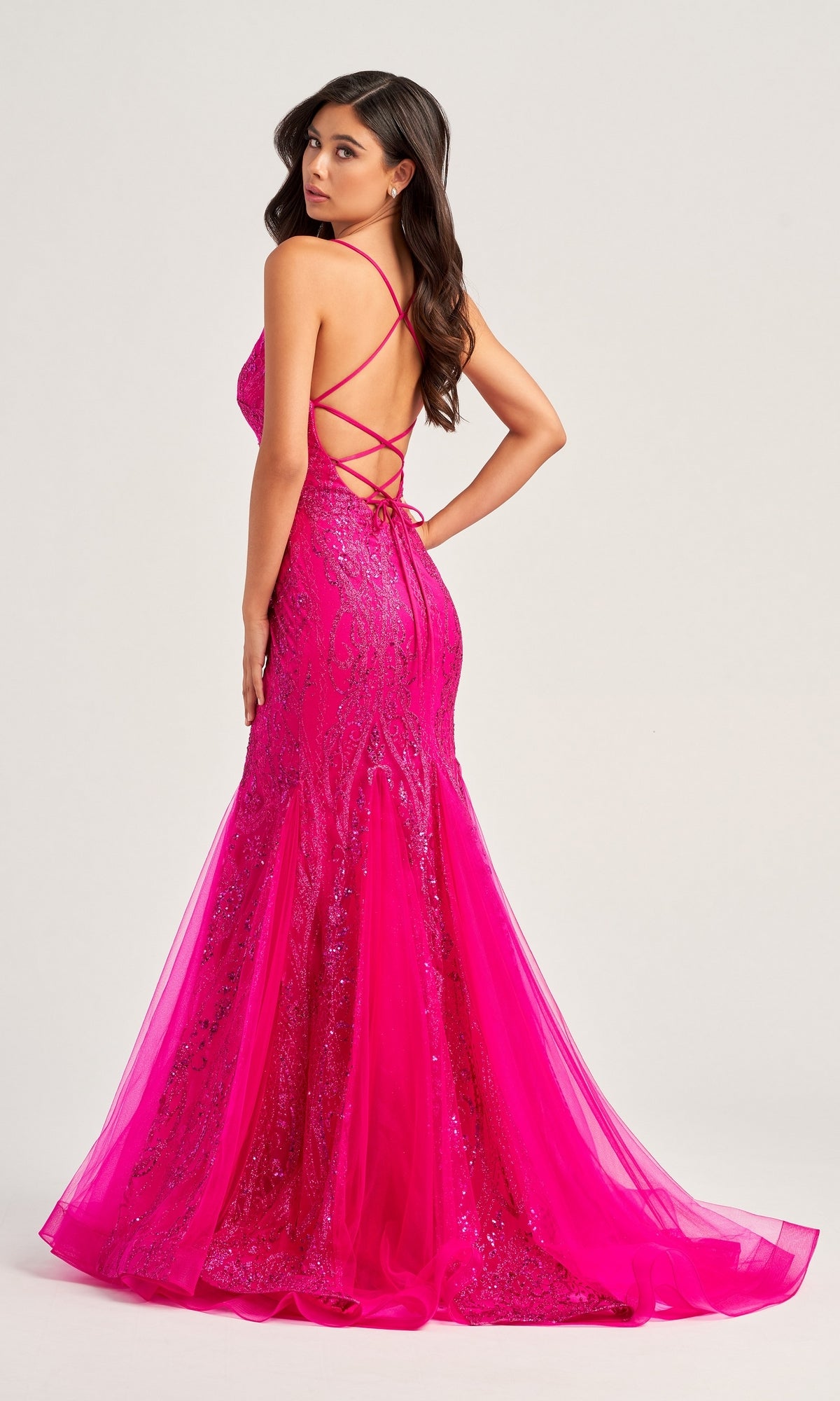 Woman wearing the Colette Long Glitter Mermaid Prom Dress CL5109, a bright pink, floor-length sequined gown with a fitted mermaid silhouette and open lace-up back, posing elegantly turned to the side.